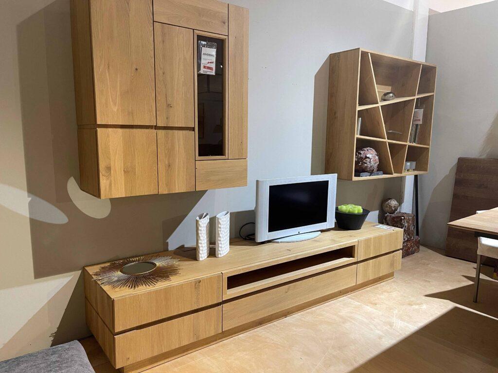 Wohnzimmermöbel aus massiver Eiche, bestehend aus einem niedrigen TV-Board mit Schubladen, einem Hängeschrank mit Glaselement, und einem offenen Wandregal mit versetzten Fächern. Auf dem TV-Board steht ein kleiner Fernseher, eine schwarze Schale mit grünen Äpfeln sowie zwei weiße Vasen. Dekorationsartikel befinden sich auch im Wandregal.
